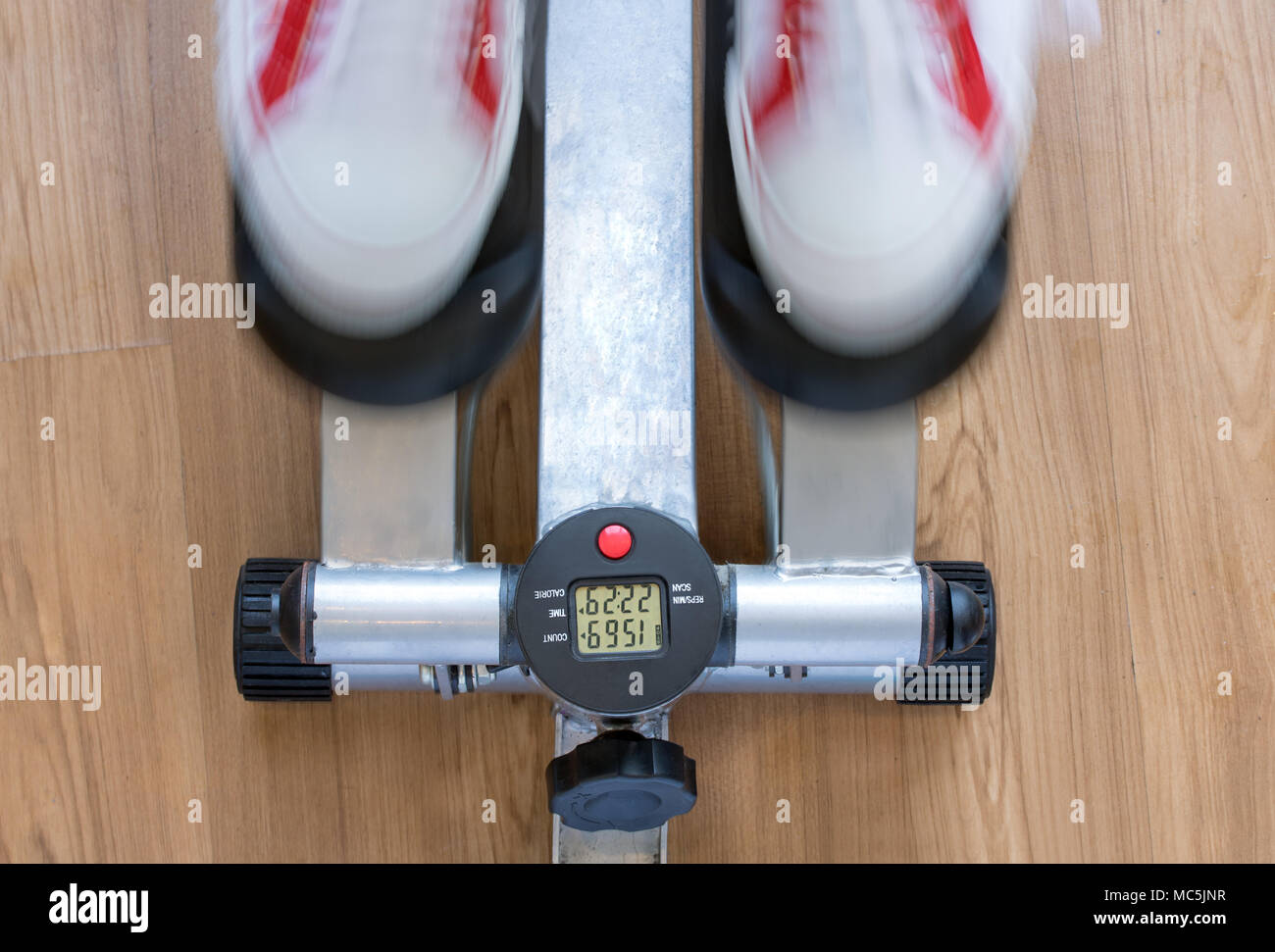 Exercise on a stepping machine, looking from above. Active person with sport shoes exercising on stepper on wooden floor, close up. Stock Photo