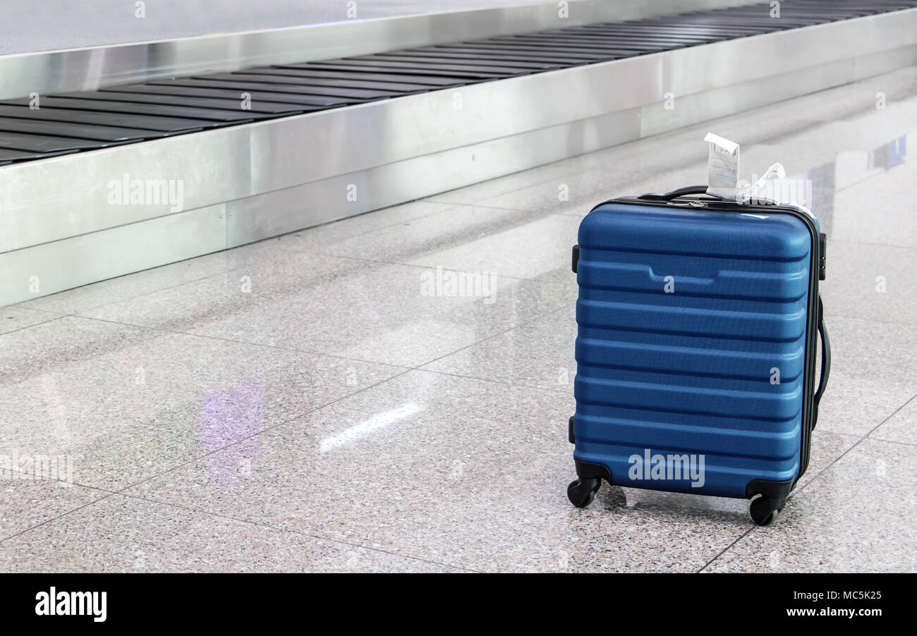 A forgotten lost suitcase in the airport hall. One case stands on wheels at the luggage transporter belt. Stock Photo