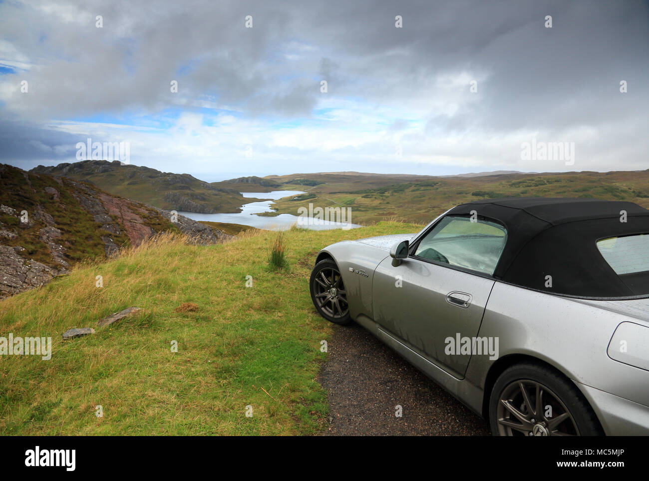 A silver sports car parked at a viewpoint in the highlands of Scotland, uk. Stock Photo