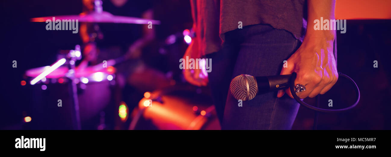 Female singer holding microphone with drummer performing in illuminated nightclub Stock Photo