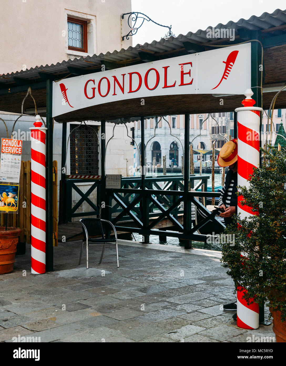 Venice, Italy - March 28th, 2018: Gondolier relaxes next to a sign advertising gondola riding Services Stock Photo