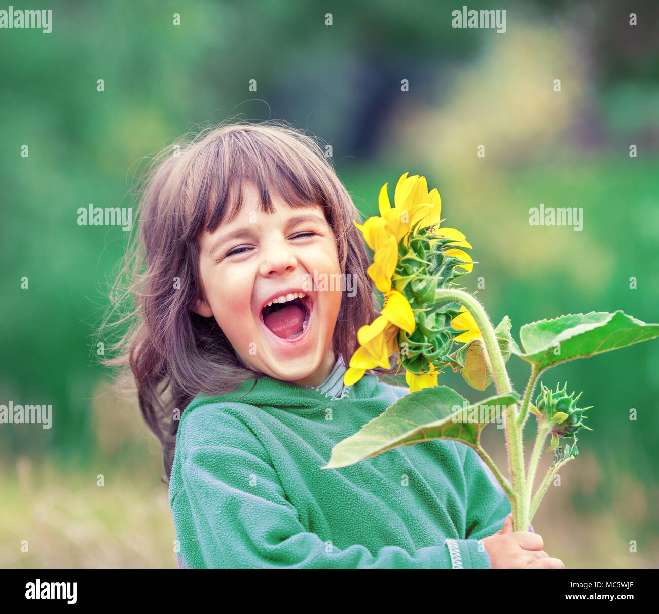 Happy laughing little girl with sunflower outdoors in summer Stock Photo