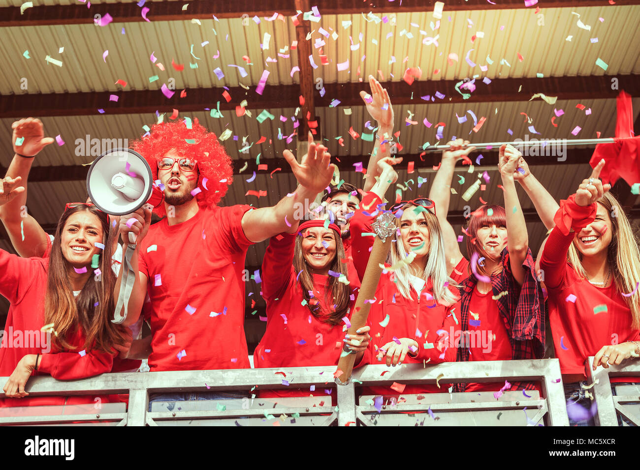 group of fans dressed in red color watching a sports event in the