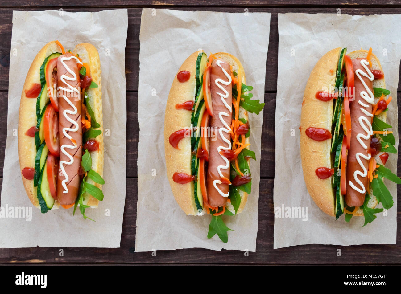 Home made hot dogs with vegetables, juicy sausage and arugula on the wooden background. The top view Stock Photo