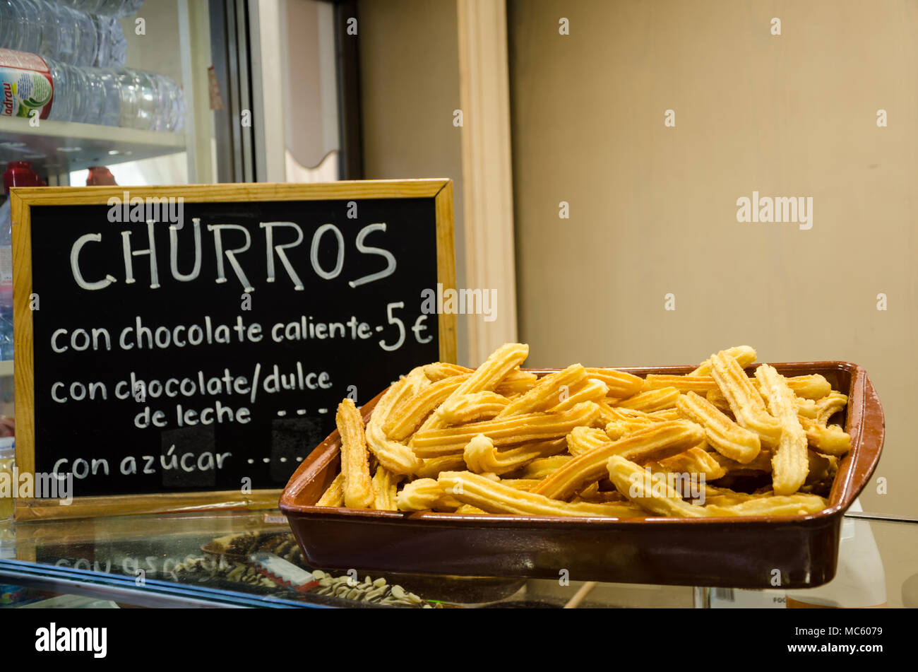 A large dish of churros and a blackboard with prices advertises the snack for sale. Stock Photo