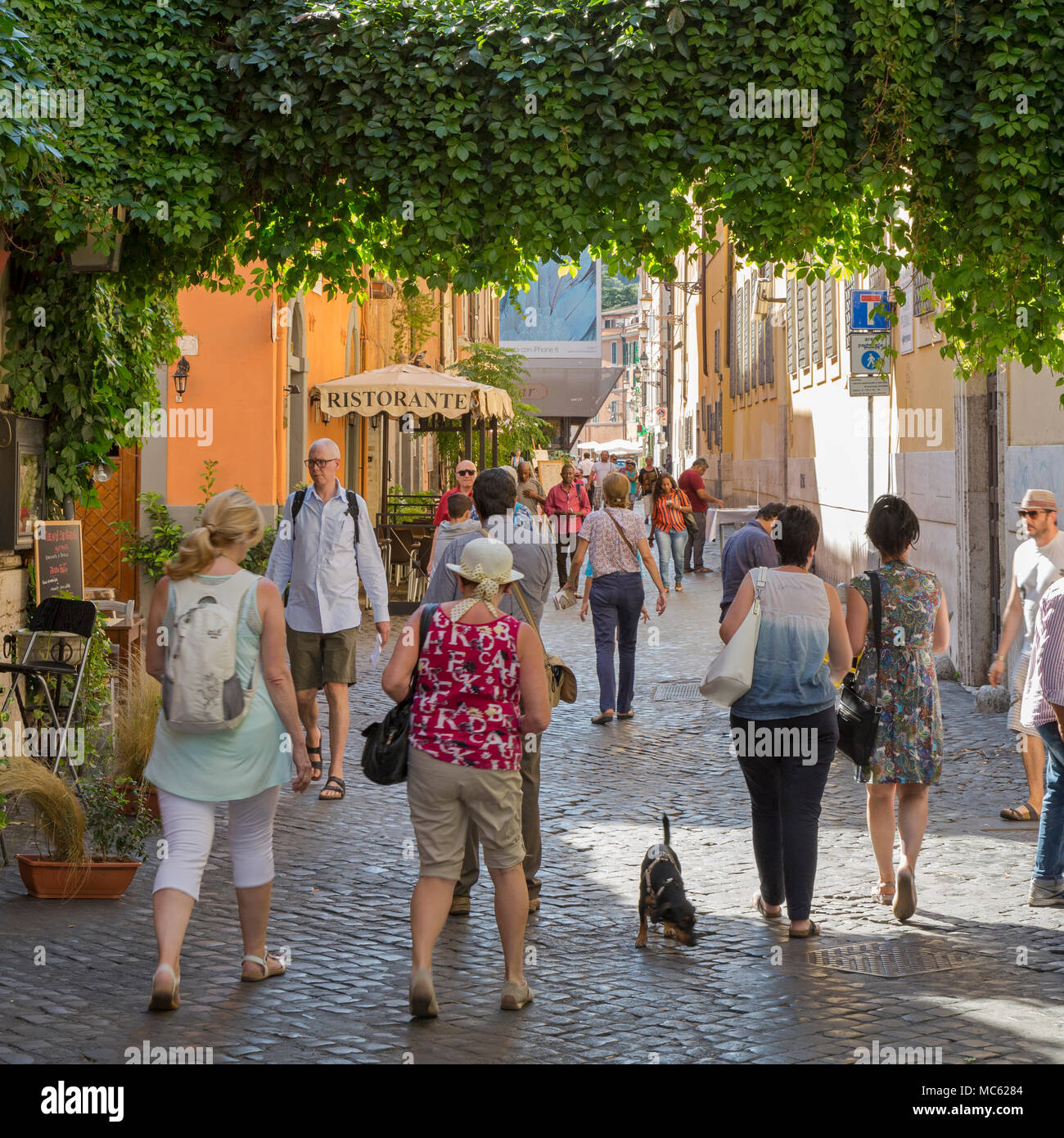 People walking down a cobbled street past restaurants with outdoor