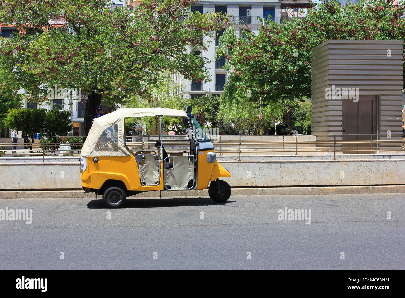 Tuk tuk small passenger three weel mini car isolated on summer empty street road background. Bright yellow rickshaw driven by locals on the street Stock Photo