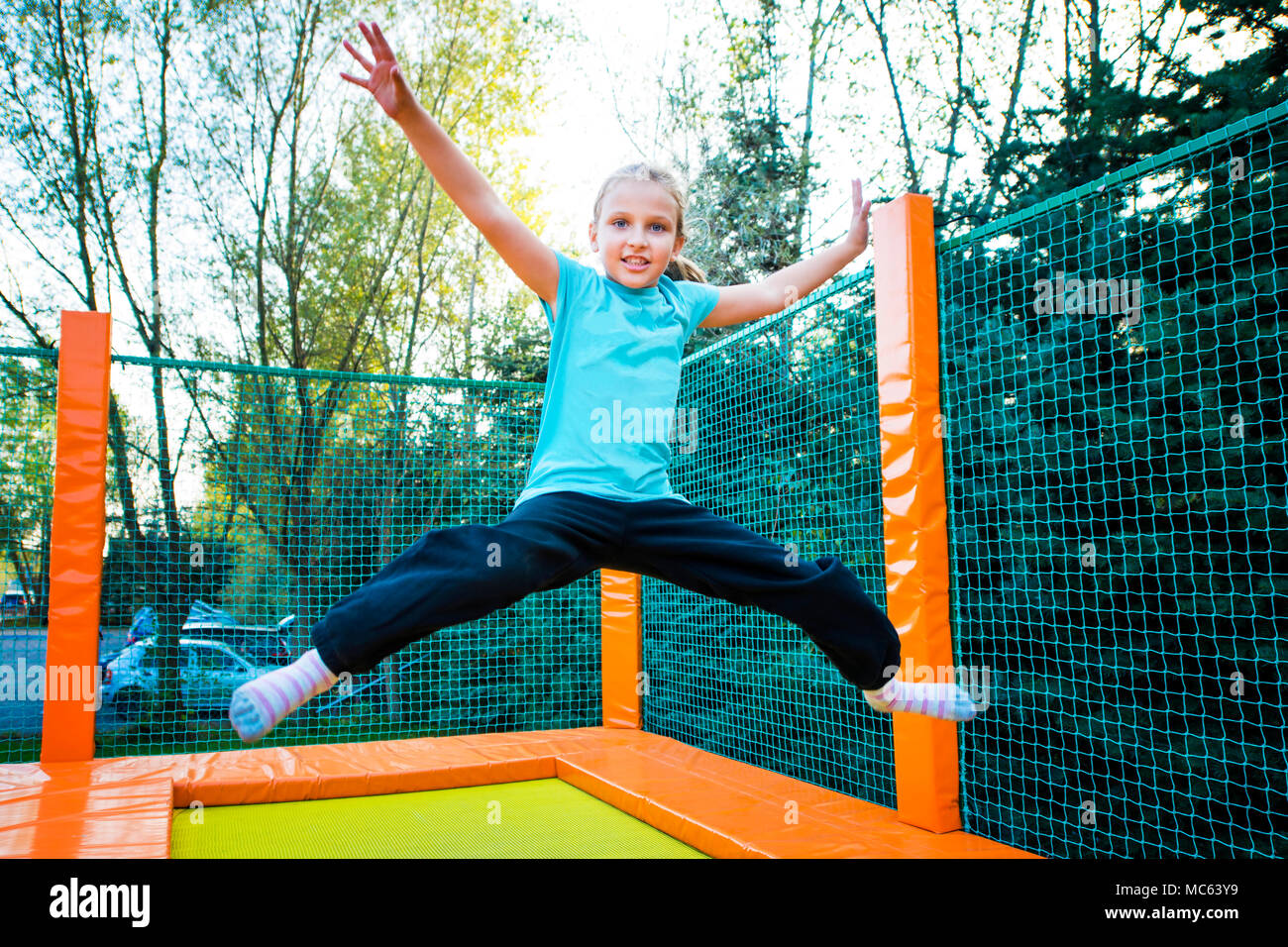 Happy caucasian girl jumping high on a trampoline on a sunny day outdoors. Stock Photo