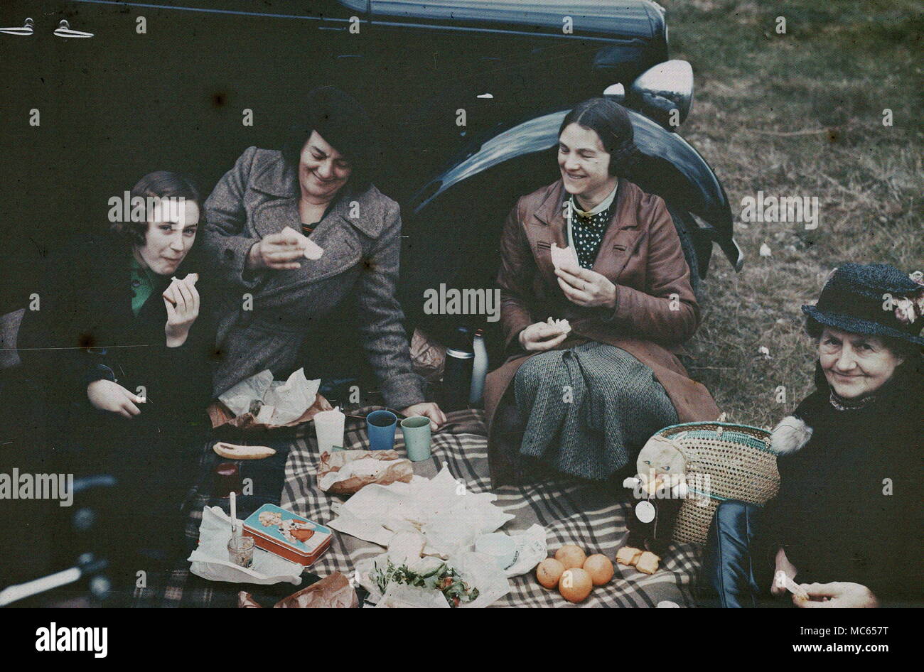 AJAXNETPHOTO. 1930S (APPROX).LOCATION UNKNOWN. - EARLY 20TH CENTURY COLOUR PHOTOGRAPHY - A GROUP OF WOMEN ENJOYING A PIC-NIC LAID OUT ON A TARTAN RUG WITH A CAR IN THE BACKGROUND. MADE WITH DUFAY COLOUR FILM. PHOTOGRAPHER:UNKNOWN © DIGITAL IMAGE COPYRIGHT AJAX VINTAGE PICTURE LIBRARY SOURCE: AJAX VINTAGE PICTURE LIBRARY COLLECTION REF:DUF 1930 08 Stock Photo