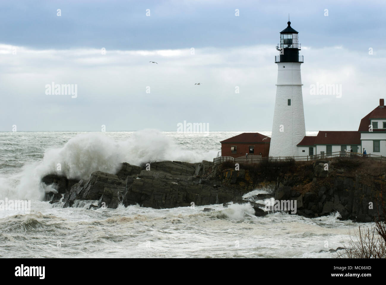 Sun breaks through the storm clouds as huge waves crash by Portland Head lighthouse in Maine during high tide. Stock Photo