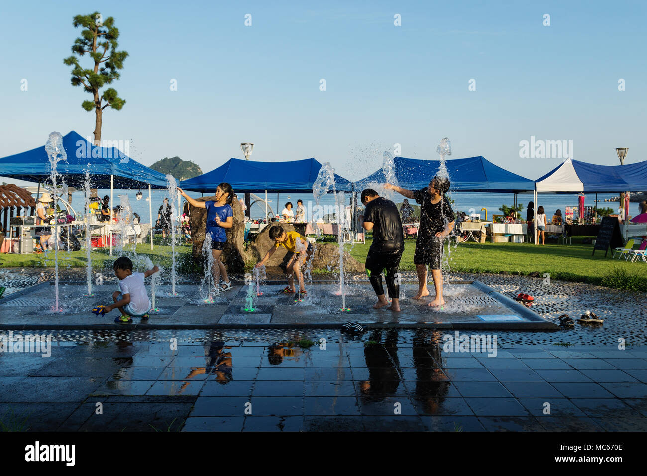 Seogwipo, Jeju Island, Korea - August 27 2017: Kids playing at a fountain at the coast in front of souvenir stands Stock Photo