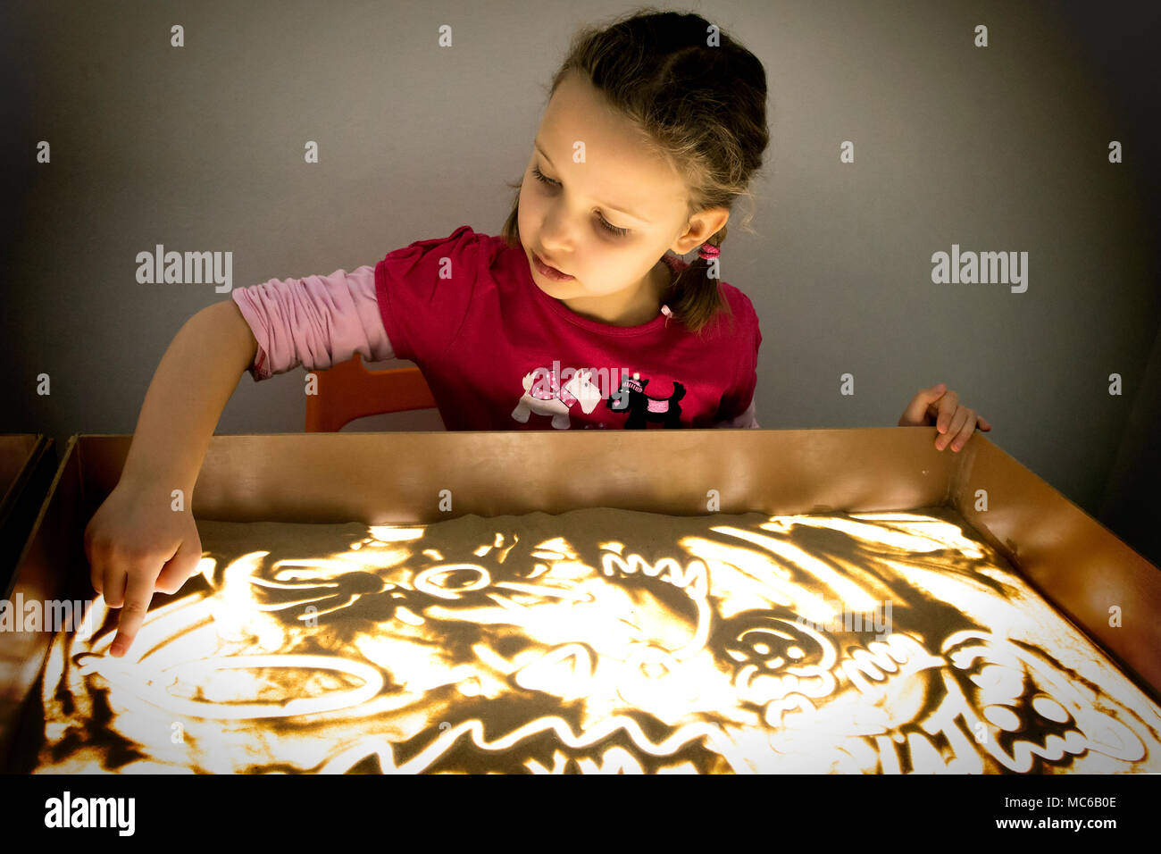 Child girl draws with sand on a light table. Stock Photo