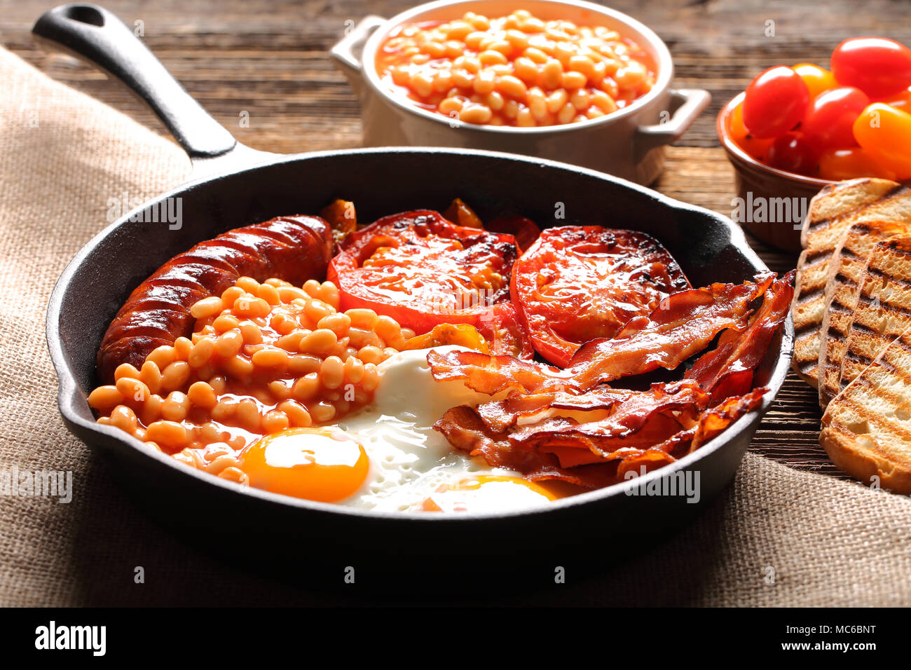 English Breakfast with sausages, grilled tomatoes, egg, bacon and beans on frying pan Stock