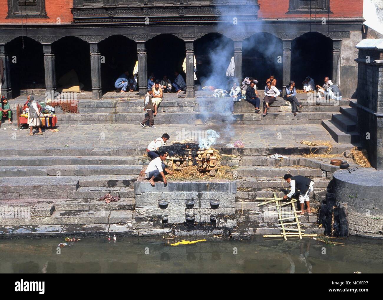 Hindu cremation Cremation of a dead body by the Bagmati river (Kathmandu valley). The corpse, removed of its clothing beneath the straw, is burned. Theshes are then thrown into the river. Stock Photo