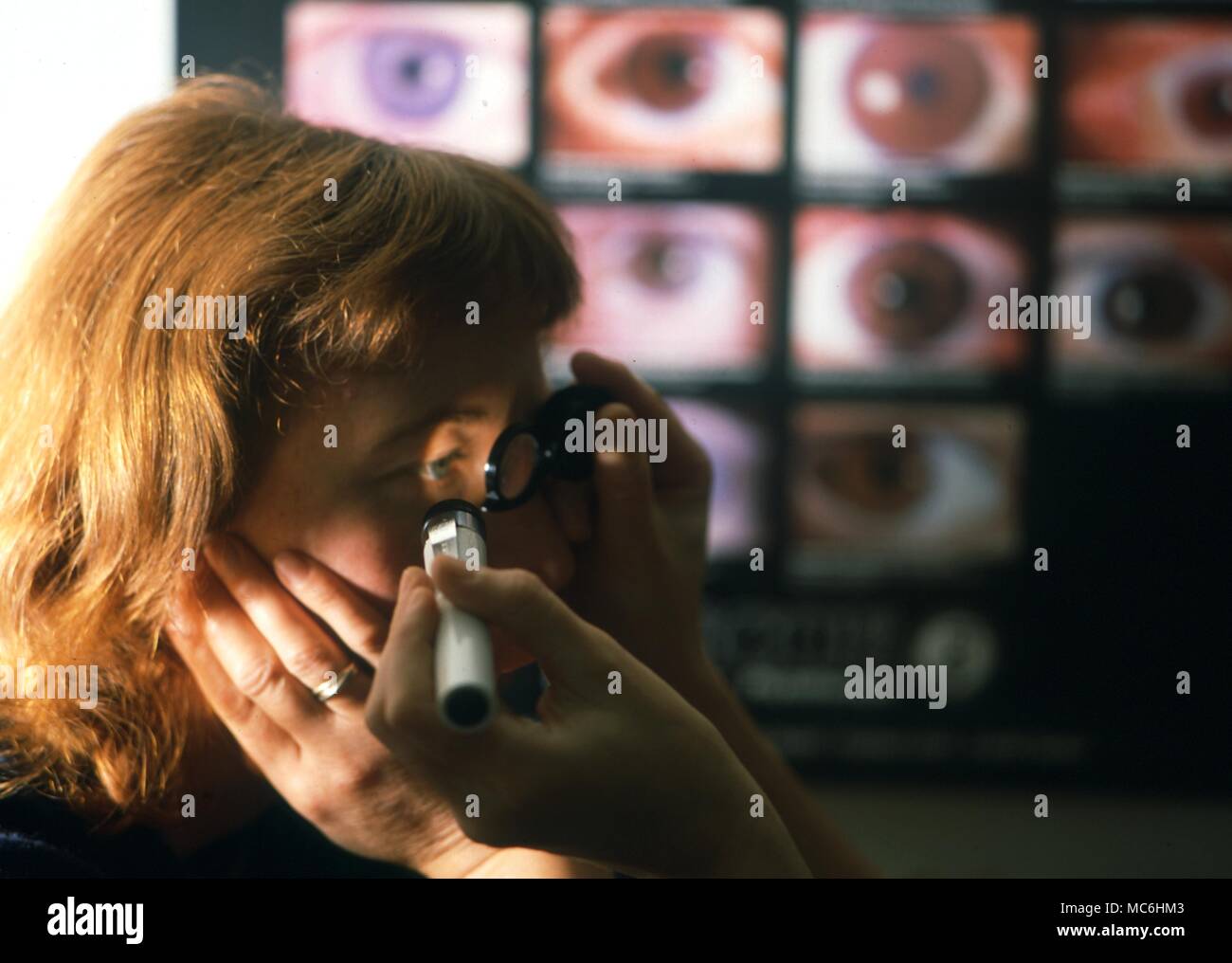 Iridology. Examining the eye of a patient against a background of iris images. Stock Photo