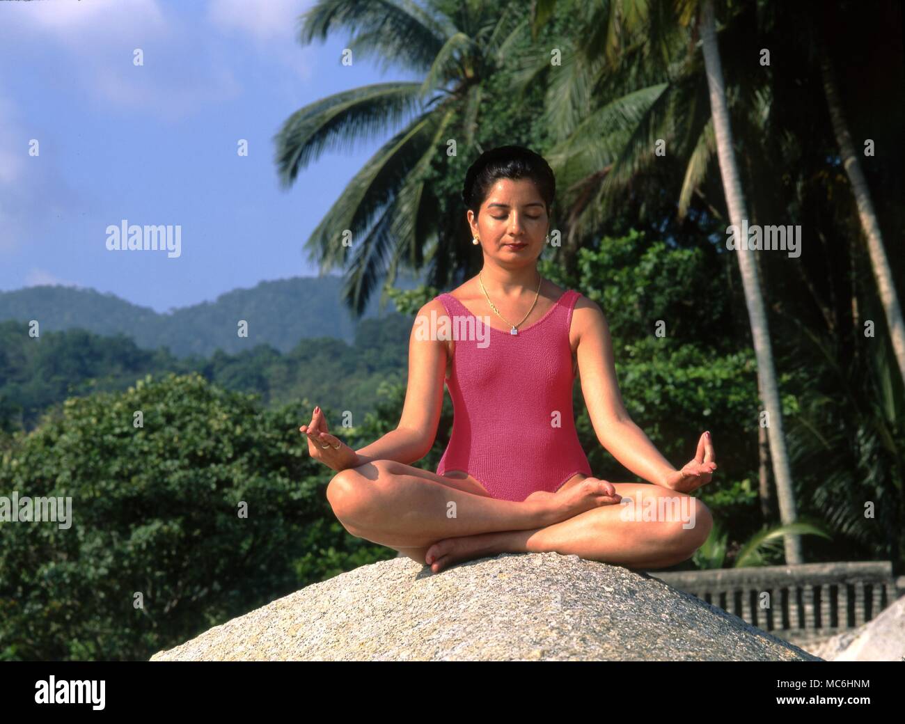 Indian lady meditating on a rock beneath a palm tree. Stock Photo