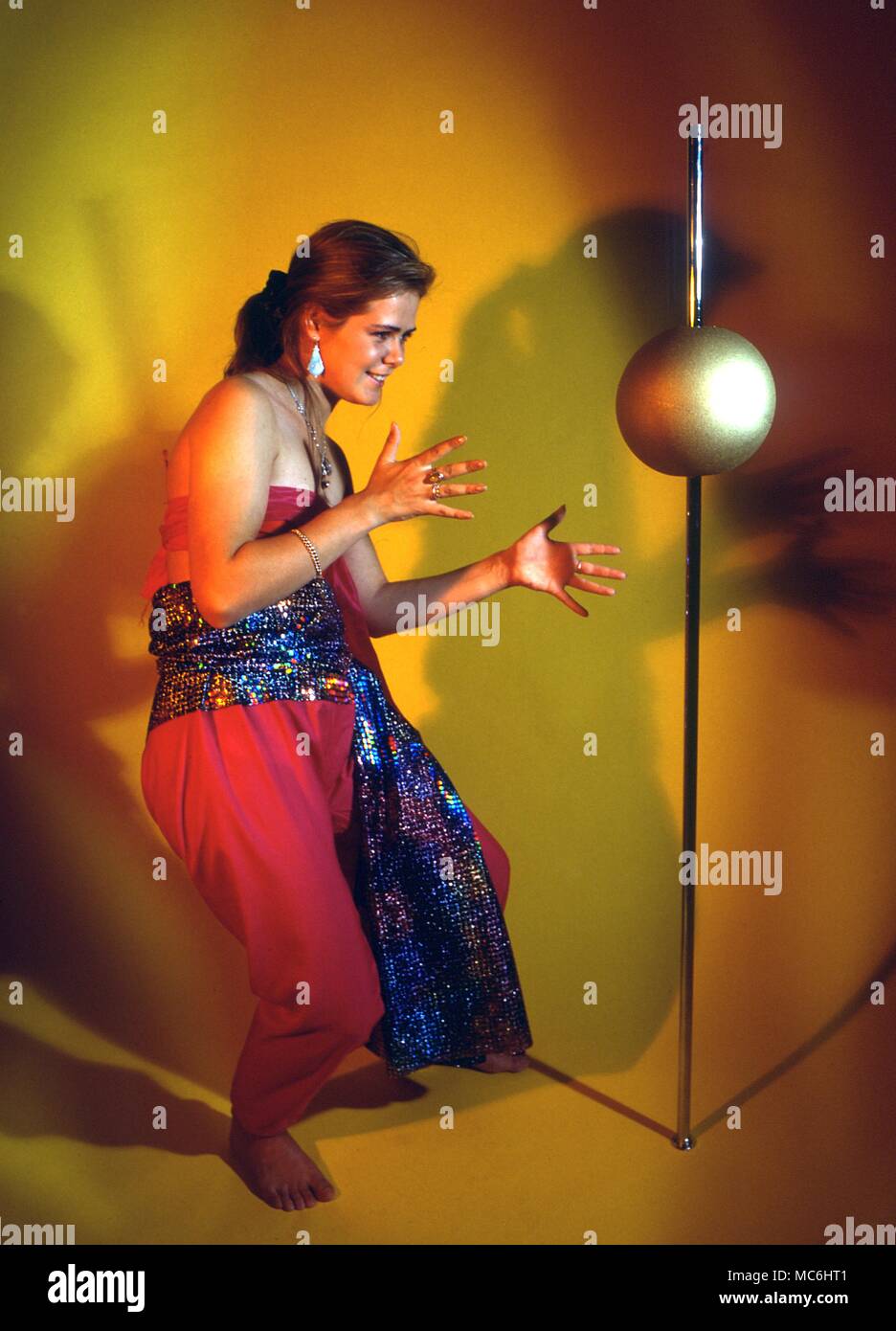 Stage Magic - The Animated Ball. The girl shows that the ball has a hole through it. She slips it over the pole and it slides to the floor. Slowly, under her mesmerizing influence, the ball rises and falls to her command. Stock Photo
