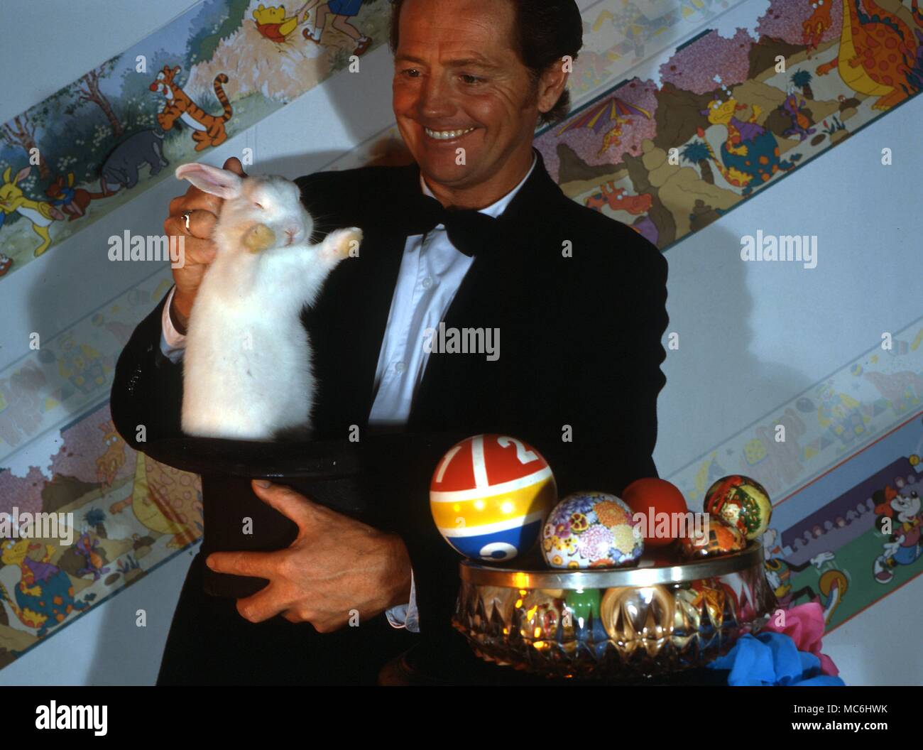 The magician lifts a white rabbit from a top hat which has just been shown to be empty. Stock Photo