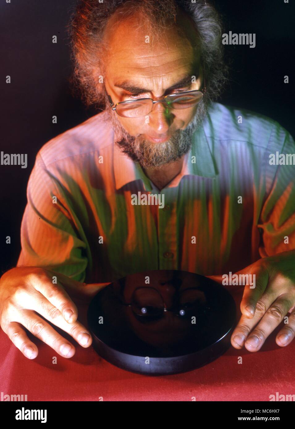 Scrying. Man looking into a scrying glass or speculum with polished black surface. It is used as an autoscope for the projection of pictures from the mind. Stock Photo