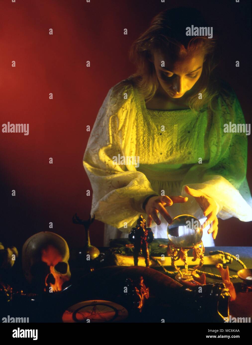 Crystal gazing. Clairvoyant with a crystal ball on a table upon which is displayed a number of ritual objects. Stock Photo