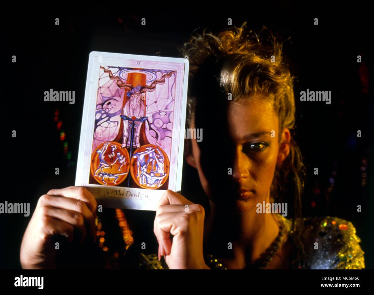 Tarot Cards Woman holding up the Tarot card, The Devil, from the deck