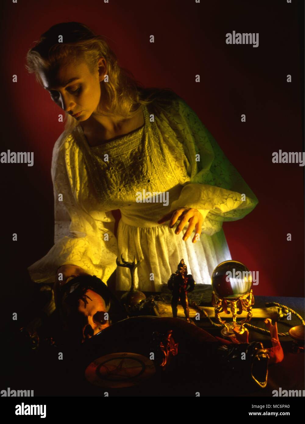 Young woman preparing for a wiccan ritual, arranging ritual objects, which include such things as a human skull, shaman trumpet, incense burners, and so on. Stock Photo