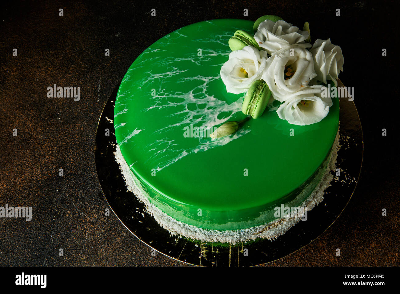 top view of homemade mousse cake decorated with green mirror glaze, white roses, coconut chips and macaroons Stock Photo