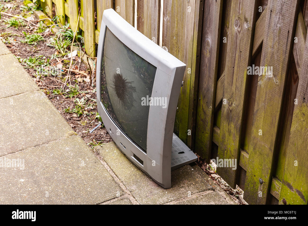broken TV placed against a wooden fence Stock Photo