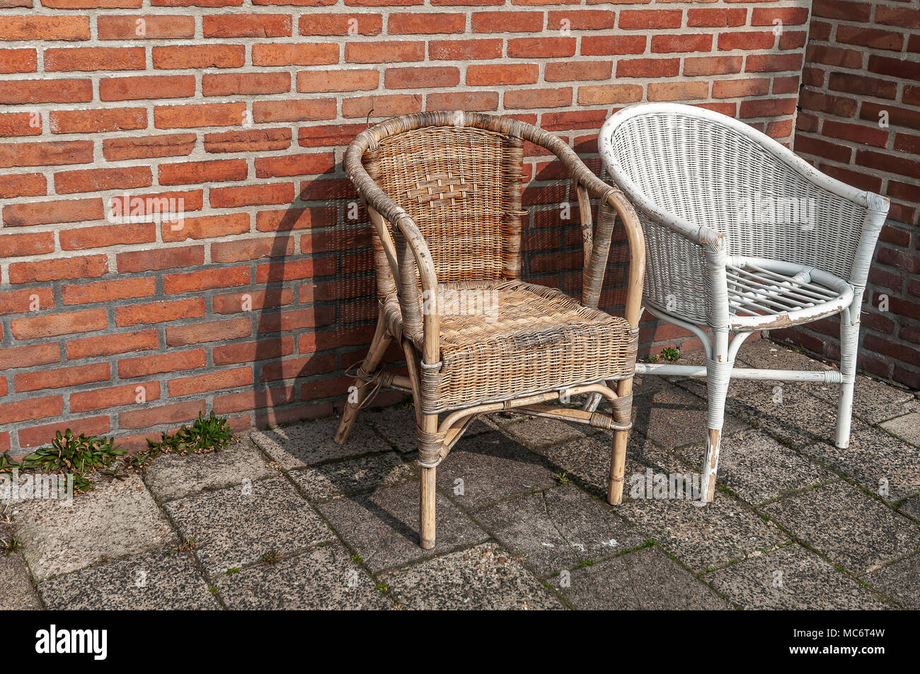 two worn wicker chairs placed in front of a stone wall Stock Photo