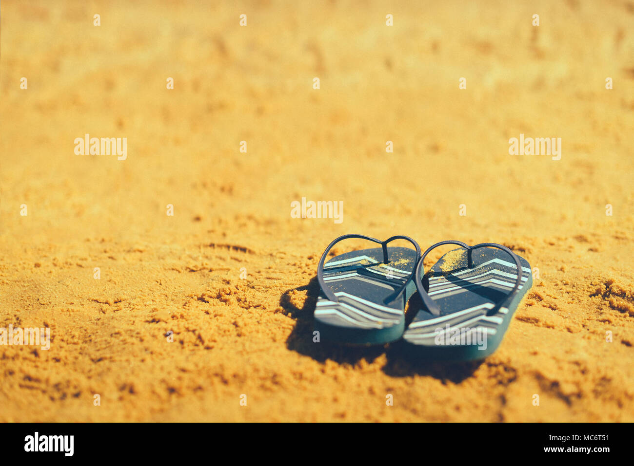Summer slippers. Navy blue flip flop on yellow sand beach background ...