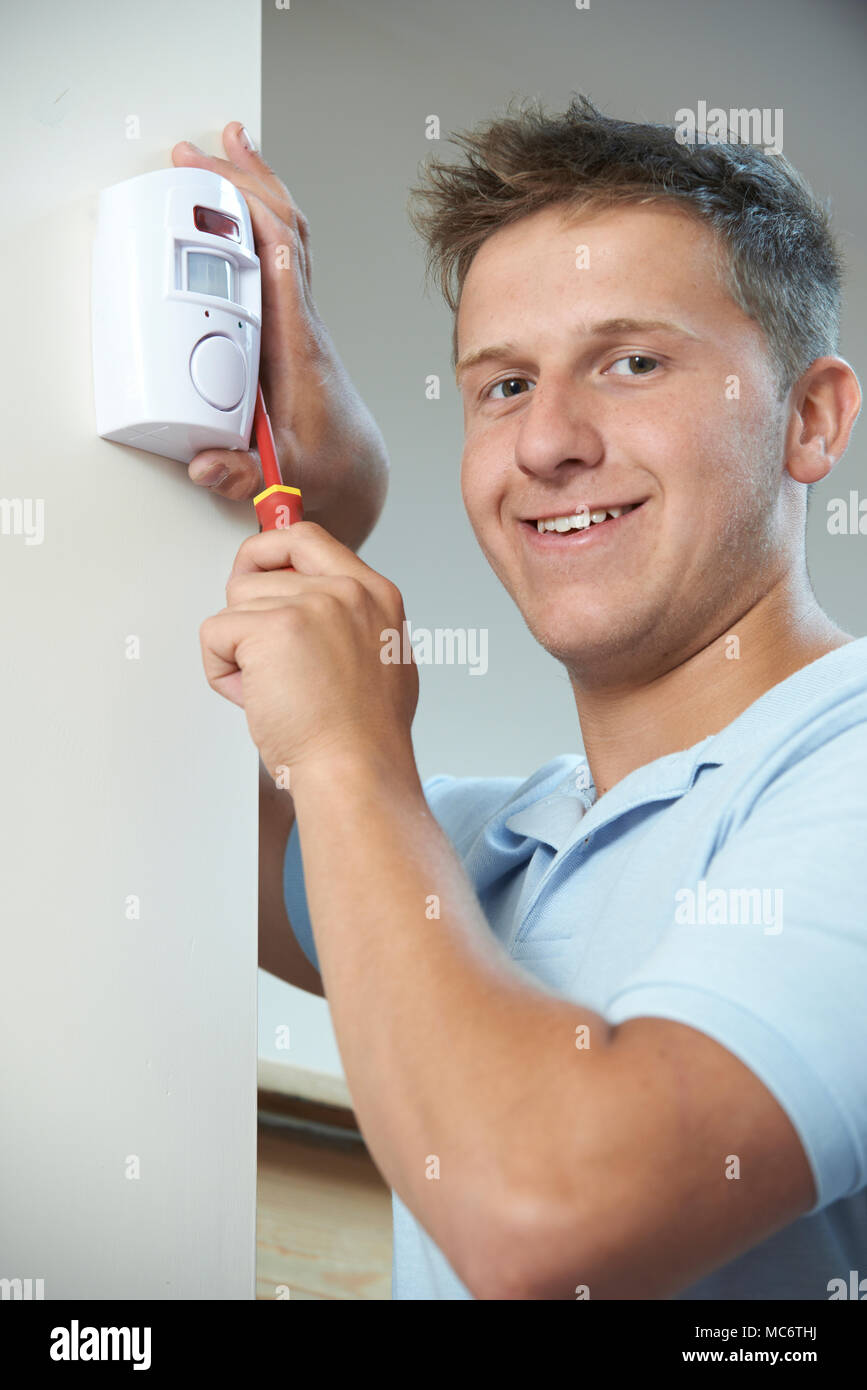 Portrait Of Security Consultant Fitting Burglar Alarm Sensor In Room