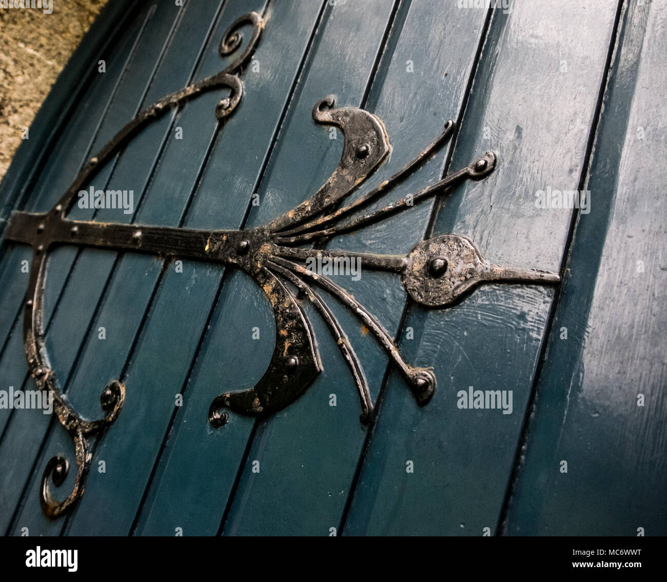 Massive Church door hinge in black painted wrought iron work on dark blue door, a bit like a bow and arrows design. Stock Photo