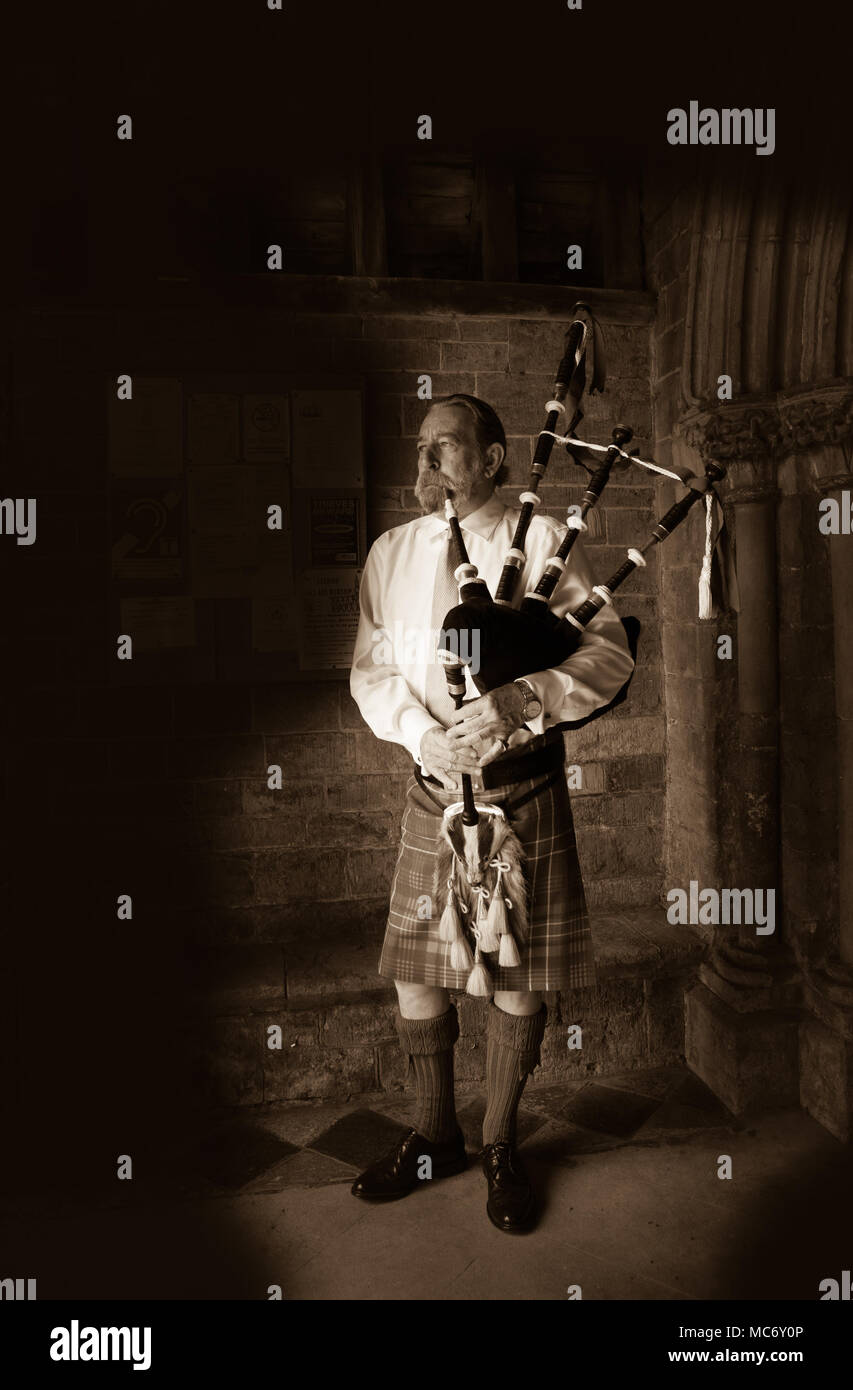 Sepia image of standing Scottish piper, in full traditional highland dress, playing the bagpipes in the doorway of Swalcliffe Church Oxfordshire Stock Photo