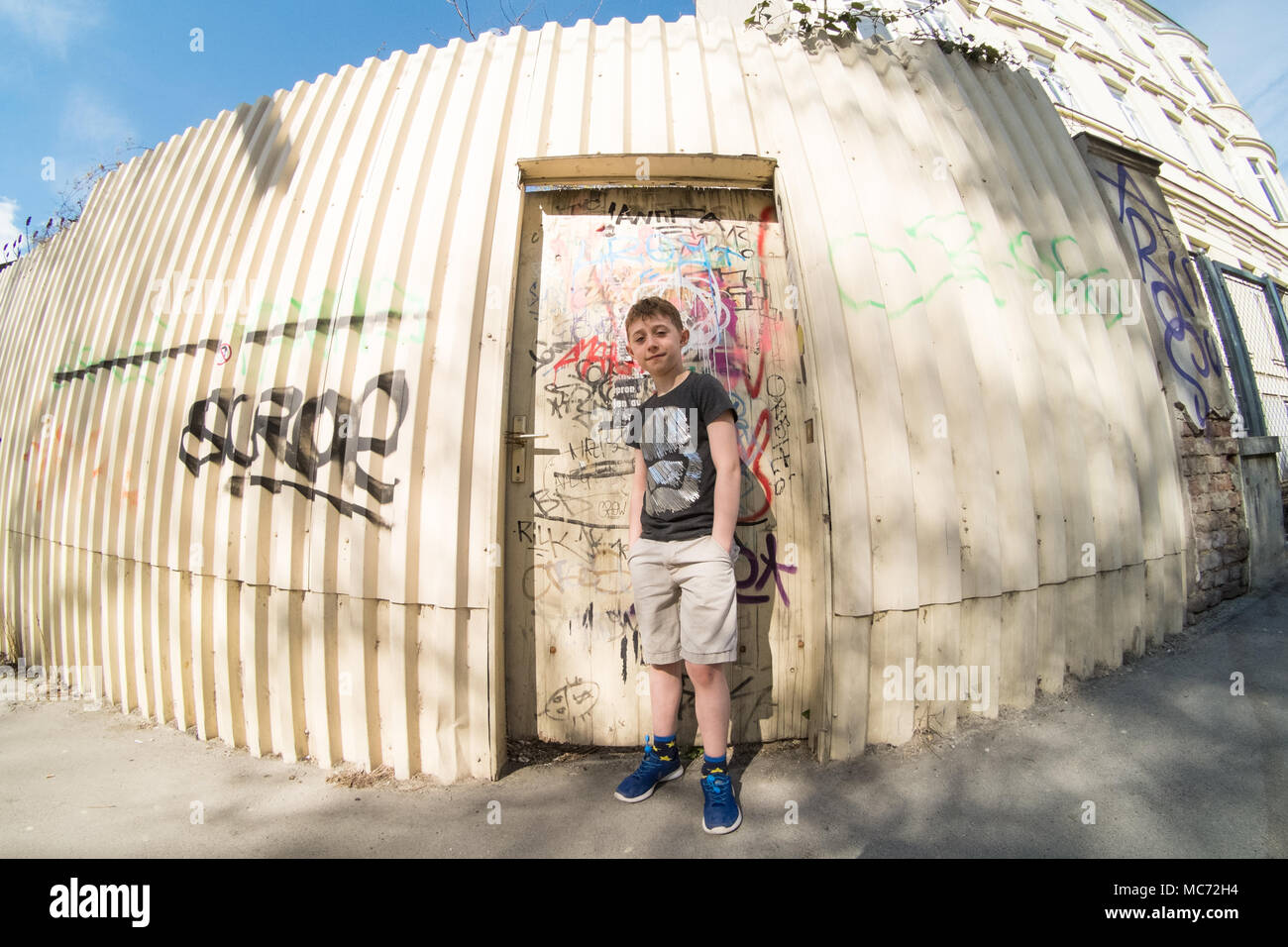 Eight year old boy standing in front of a graffiti covered doorway, Vienna, Austria, Europe. Stock Photo