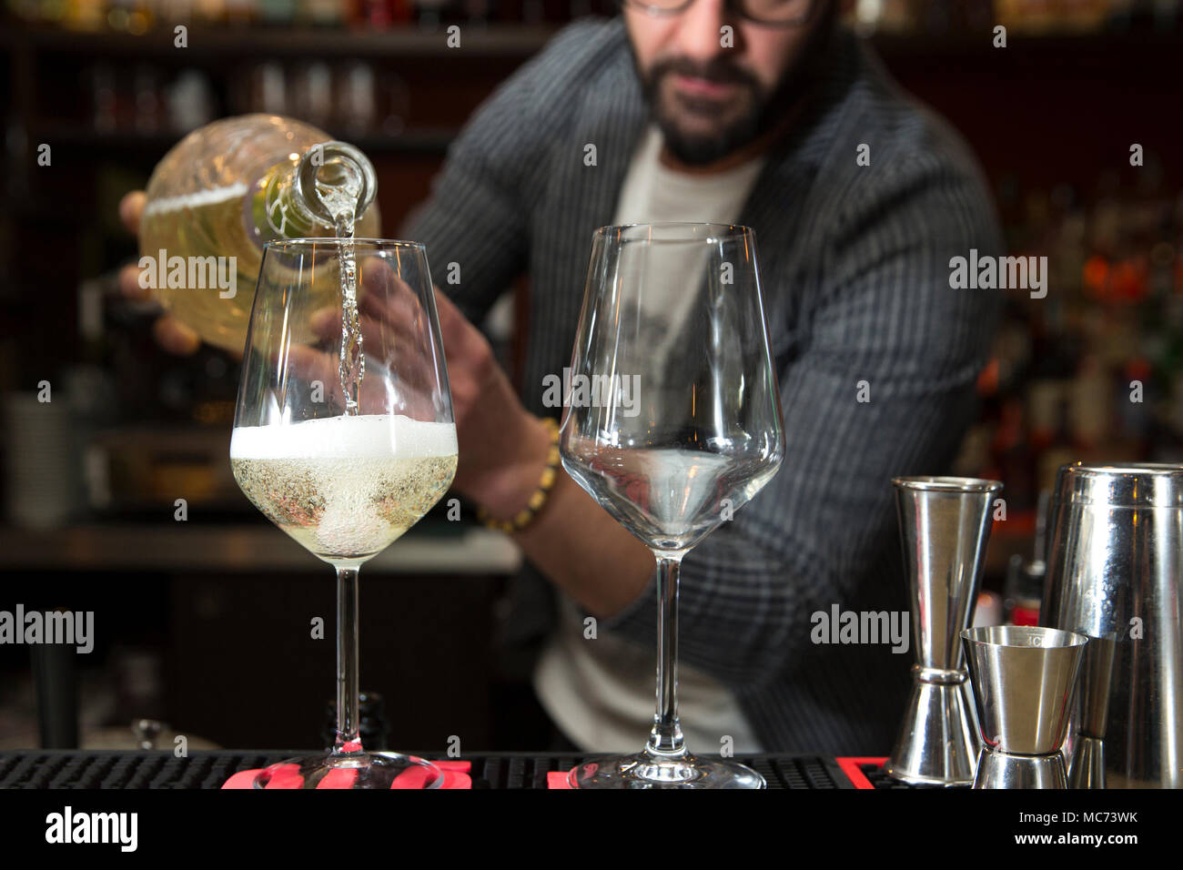 closeup of a barman working behind a bar counter, pouring prosecco in