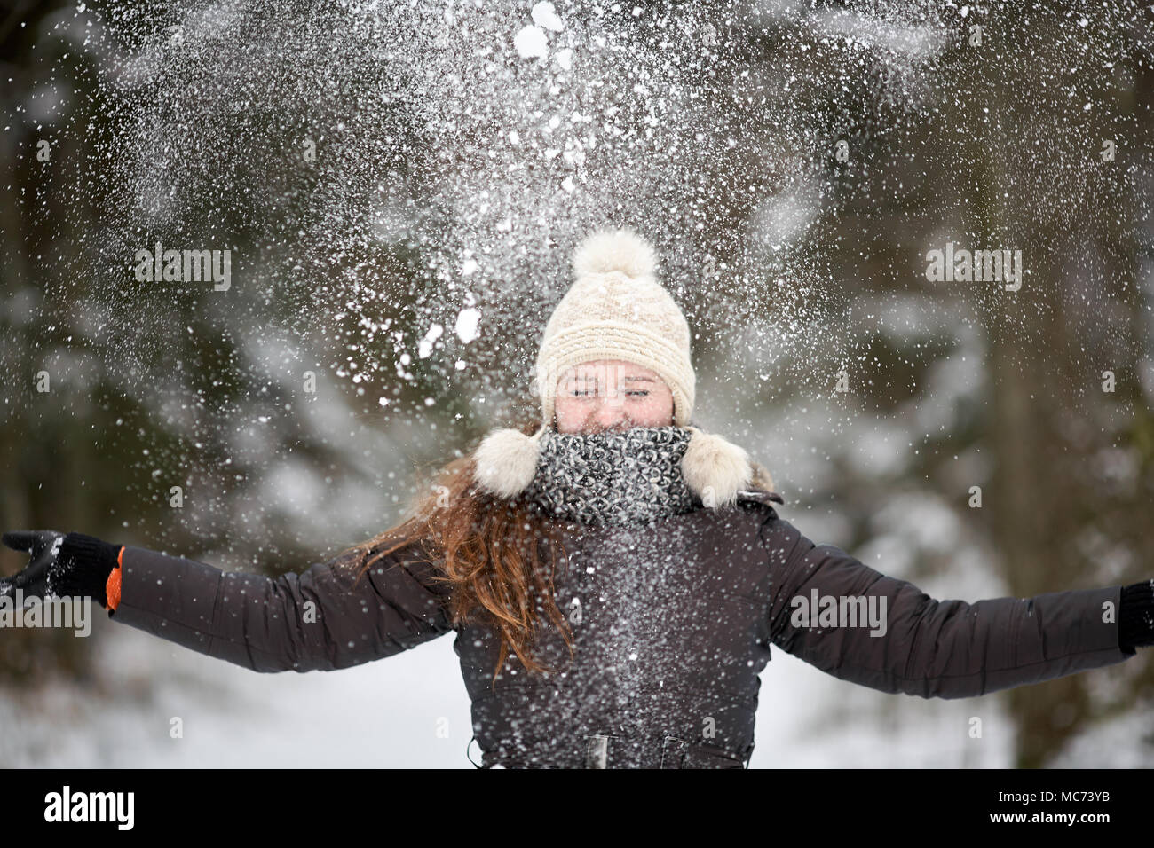 Young beautiful caucasian girl whith wihite hat  posing against a winter park background and playing with the snow Stock Photo