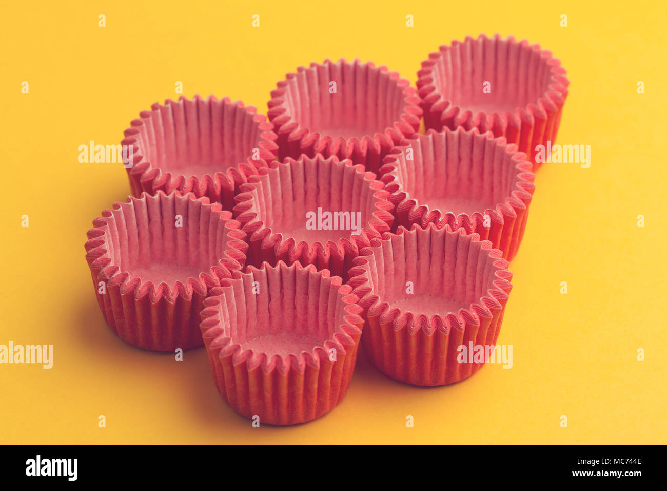horizontal top view of arrangement of many pink small paper baking tray holders for cupcakes and muffin on yellow background Stock Photo