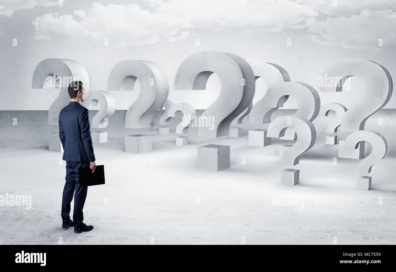 Businessman standing and looking to a bunch of question mark signs ...