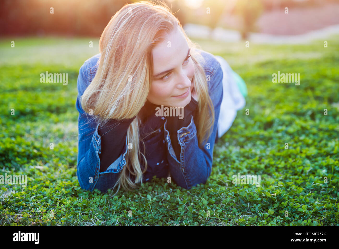 Authentic portrait of a pretty girl lying down on fresh green grass meadow, genuine beauty ofa  young woman, enjoying spring nature and peaceful weeke Stock Photo