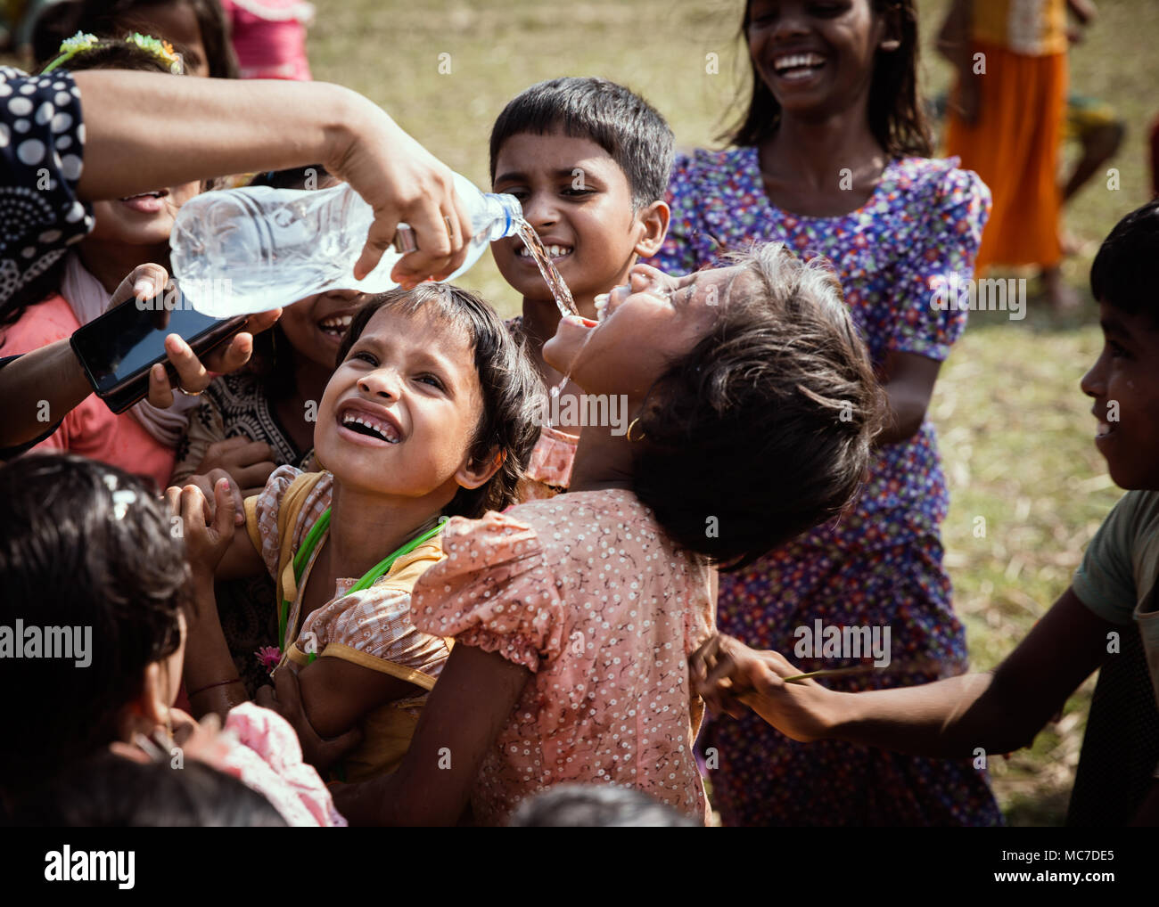 A Rohingya woman gives water to children while they play in nearby fields. There are now approximately 600,000 Rohingya refugees in the Kutupalong refugee camp of Southern Bangladesh. While preparations are now being made for the Monsoon season which is fast approaching, many NGO’s have left leaving much work to be done to make up for their shortfall. Stock Photo