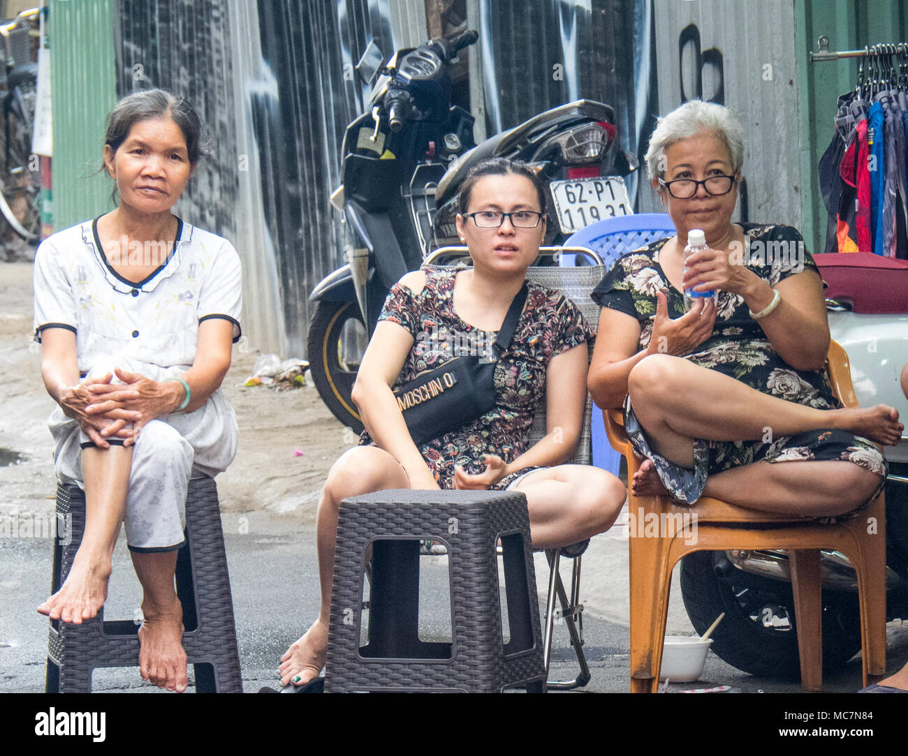 Three Vietnamese women sitting on plastic chairs on the pavement
