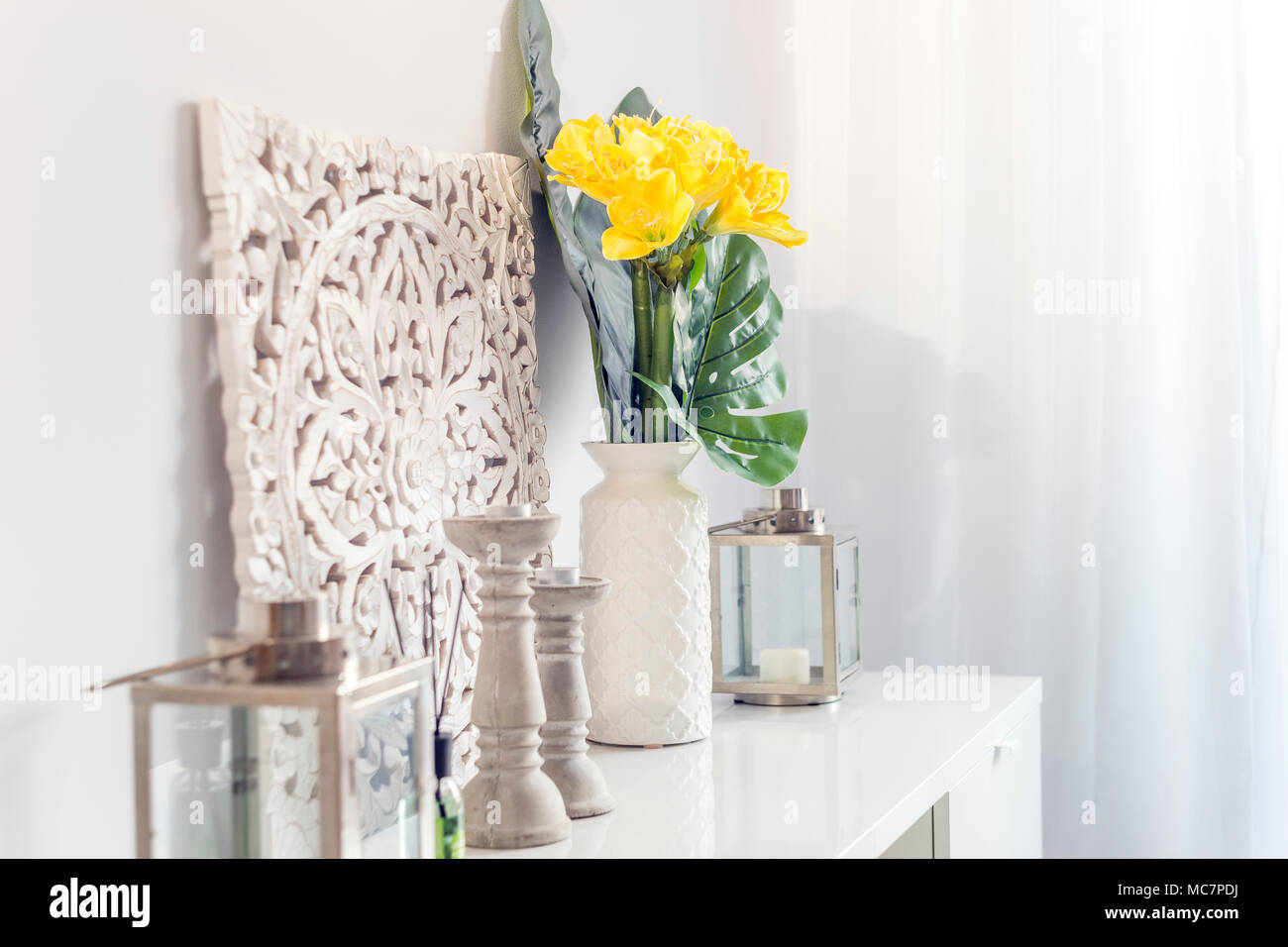 Yellow flowers in ceramic vase with wooden candlesticks and lantern decorating a shelf in a living room Stock Photo