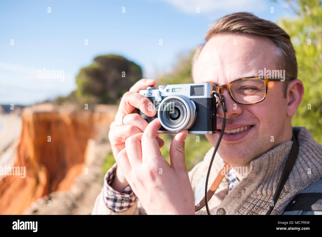 A photographer taking pictures of cliffs and ocean during sunny day with mirrorless camera Stock Photo