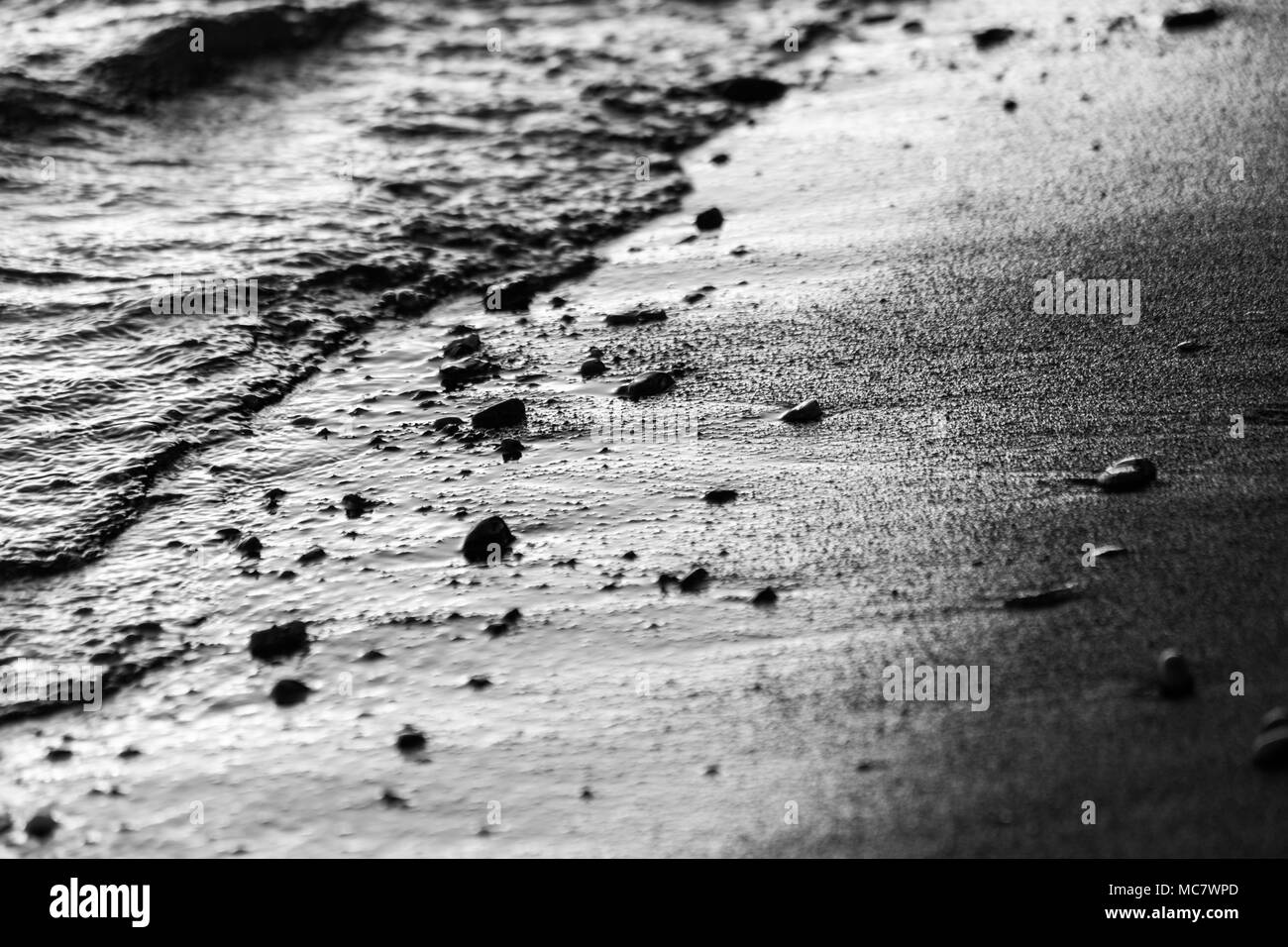 A close view of water on a lake shore at sunset, with details of sands and little round stones Stock Photo