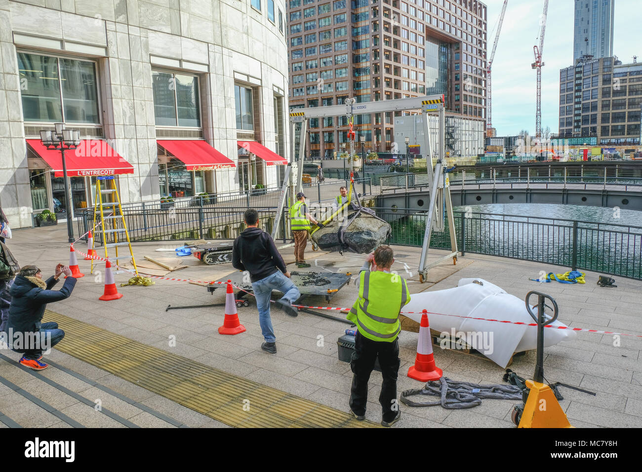 West India Quay, London, UK - March 26, 2017: Workmen in high viz jackets hoisting a large stone beside the water front. Stock Photo