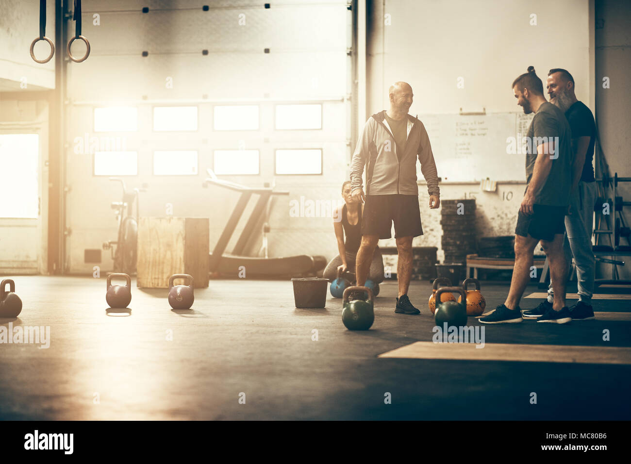 Three fit men in sportswear smiling and talking together around weights
