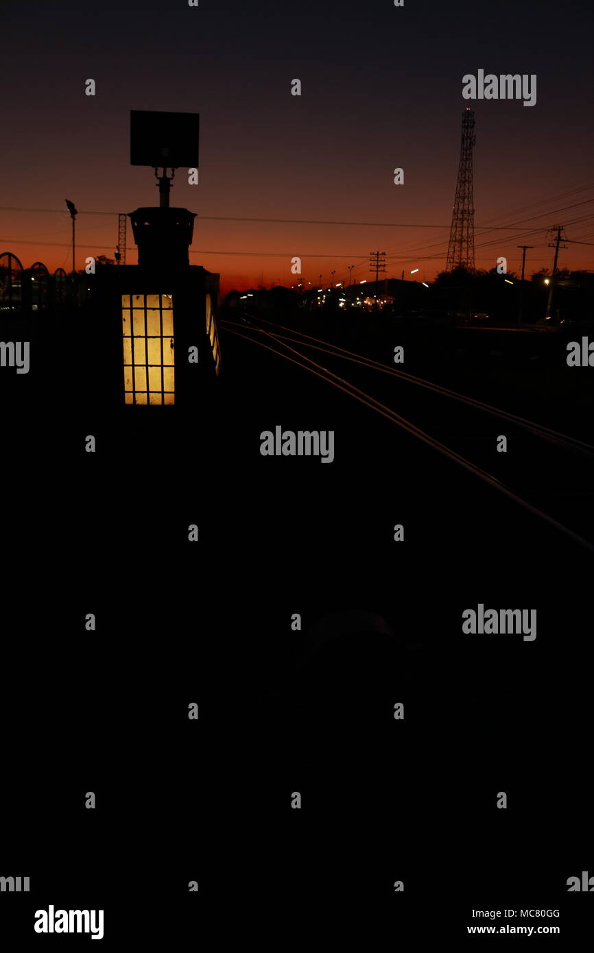 Silhouette photo, at twilight, the foreground is the yellow signal lamp of the train, The backdrop is light projected onto the railroad tracks. Stock Photo