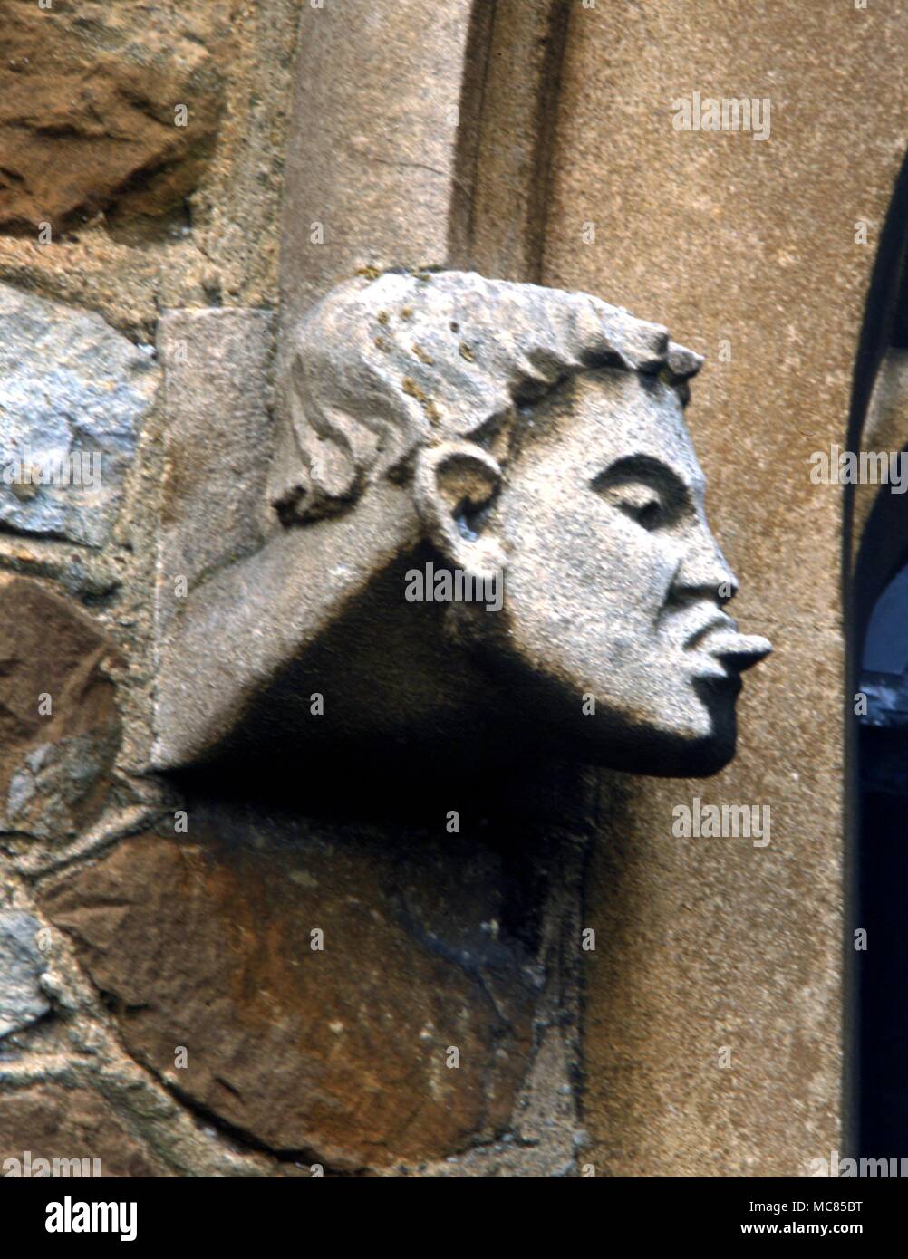 Carving of a man putting out his tongue on the south porch of Frensham church. The church was founded in the thirteenth century by Luc des Roches, and is now famous for its 'witch cauldron' which has nothing to do with witches, but was an ale cauldron, used in church festivities. Stock Photo