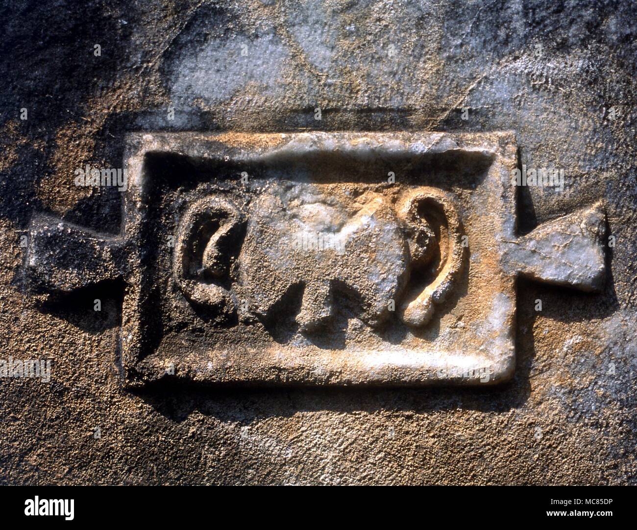 A sacred initiation symbol, of serpents in the form of ears, on either side of the Mycenean hammer-head symbol. Bas relief on the walls of the ancient Greek temple at Europas, Turkey. Stock Photo