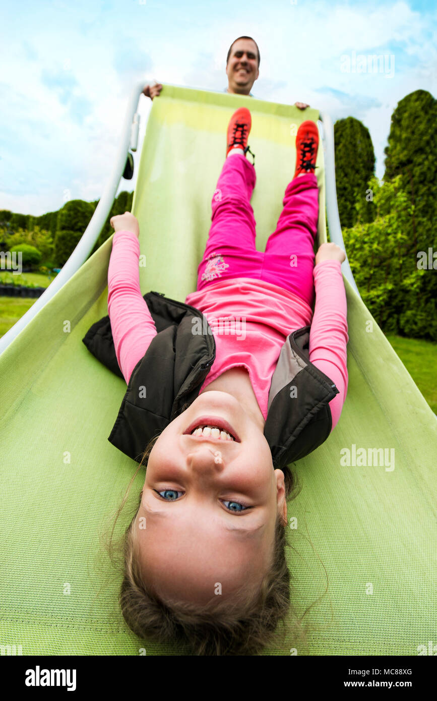 Young girl hanging upside down while her father raising hammock chair. Stock Photo
